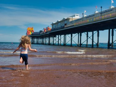 A beautiful shot of a girl running into the scene in Paignton beach, England clipart