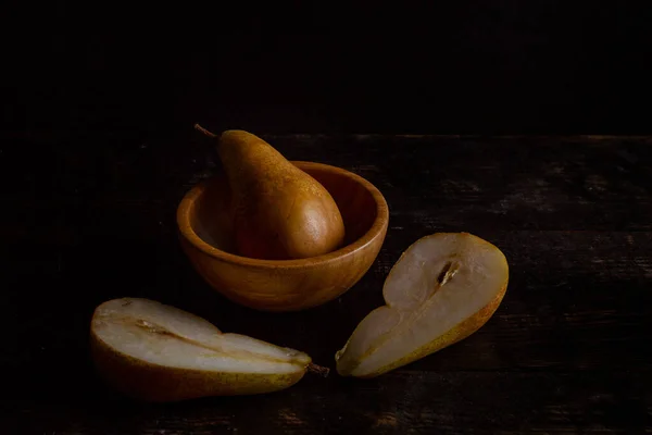 梨子在木制碗前的裂开的梨子 在深色背景上有梨子 — 图库照片