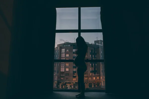 一个怀孕的女人晚上站在窗边 — 图库照片