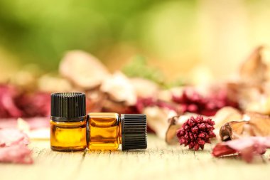 Amber essential oil sample vials close up on natural wooden surface surrounded by dried flowers. Landscape orientation. clipart