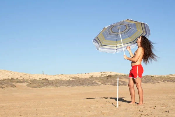 Zbliżenie Atrakcyjnego Młodego Mężczyzny Długimi Kręconymi Włosami Ustawiającego Parasol Plaży — Zdjęcie stockowe