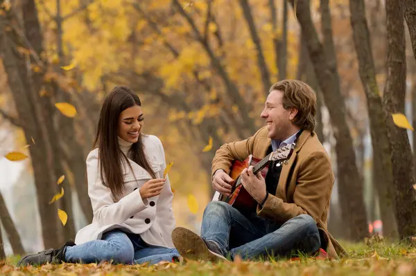 Feliz Casal Caucasiano Sentado Grama Tocando Guitarra Parque Outono — Fotografia de Stock