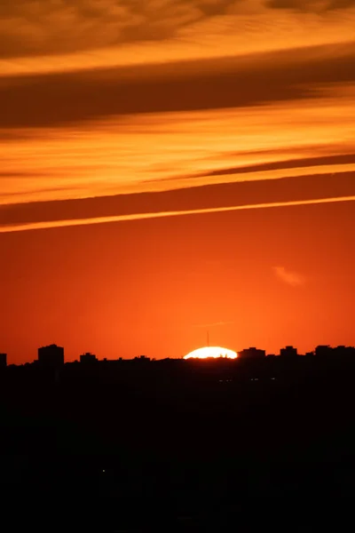 都市の建物のシルエットの後ろに隠れて太陽と壮大なオレンジ色の夕日の雲の垂直ショット — ストック写真