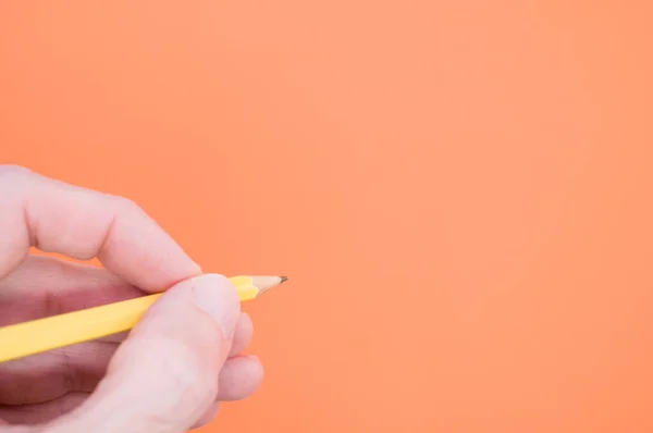 Een Hand Met Een Geel Potlood Oranje Achtergrond — Stockfoto