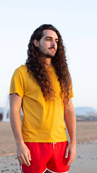Вертикальный Снимок Молодого Человека Длинными Вьющимися Волосами Стоящего Пляже — стоковое фото