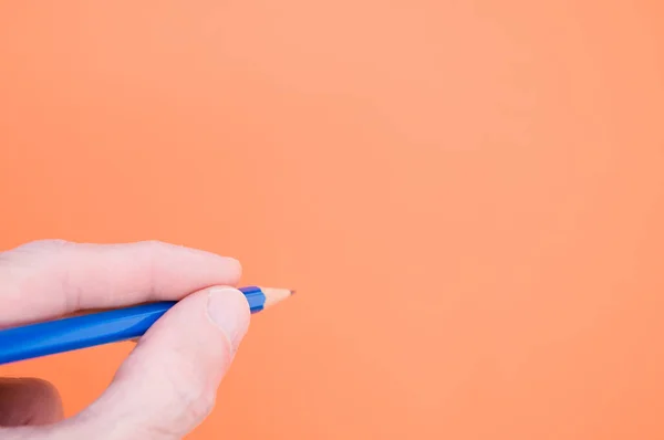 Een Hand Met Een Blauw Potlood Oranje Achtergrond Voor Een — Stockfoto