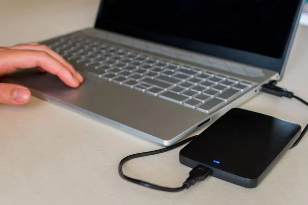 An external hard drive connected to a laptop computer on a desk. A portable hard drive. The concept of data storage.