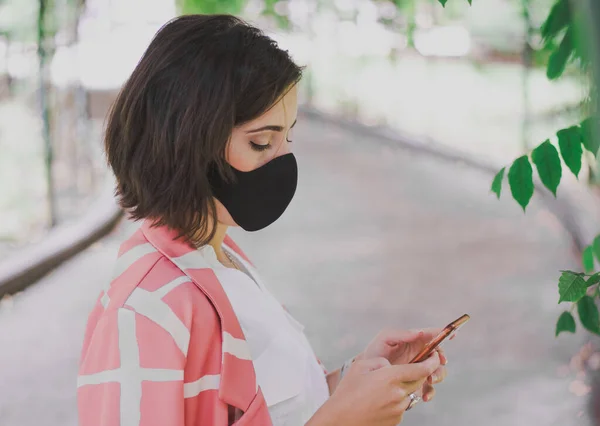 Eine Frau Blickt Auf Ihr Handy Und Trägt Eine Schutzmaske — Stockfoto