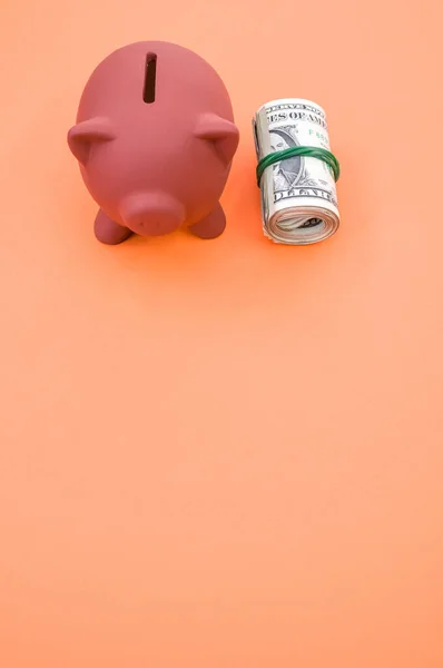 在橙色表面上垂直拍摄的美元钞票和小猪银行 — 图库照片