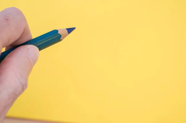 黄色の背景に青い鉛筆を持っている手のクローズアップコピースペース — ストック写真