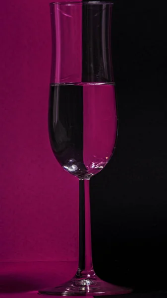 紫と黒の背景に水のガラスの垂直ショット — ストック写真