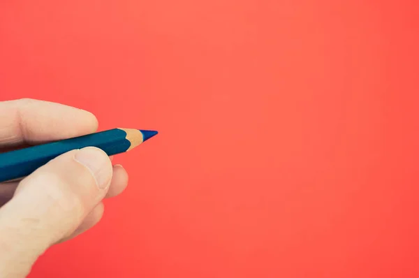 淡い赤色の背景に青い鉛筆を持っている者の閉鎖 — ストック写真