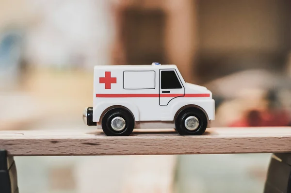 A closeup of a tiny emergency car toy placed on a wooden table on a blurry background