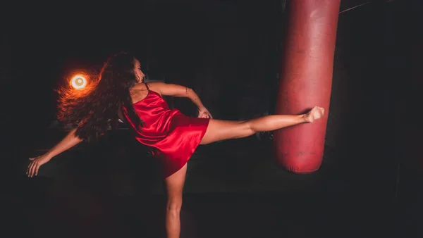 Vuxen Kvinna Röd Klänning Som Slår Boxningssäck Med Ett Ben — Stockfoto