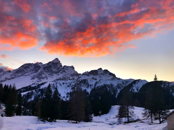 雪の壮大な景色 美しいカラフルな火の下で山の範囲をかぶった赤い夕日の雲の風景 — ストック写真