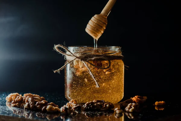 stock image The honey in a glass jar with walnuts and wooden dipper