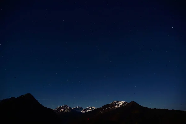 A majestic night scene in the Allgaeu Alps with the snow-capped summit and a mountain range in darkness