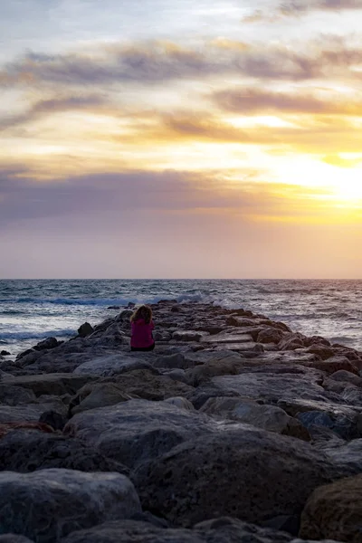 Pionowe Ujęcie Osoby Siedzącej Skałach Oglądającej Zachód Słońca Nad Morzem — Zdjęcie stockowe