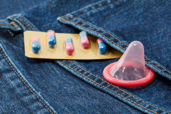 一条牛仔裤后口袋里打开的避孕套和节育药丸的头像 — 图库照片