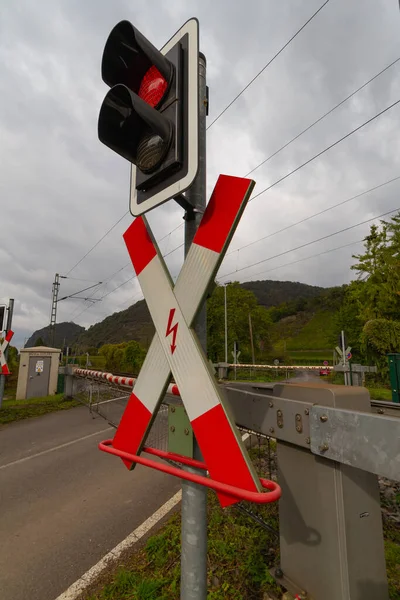 A red and white traffic sign for railroad crossing with a red stoplight in front of a green landscape and a gray sky