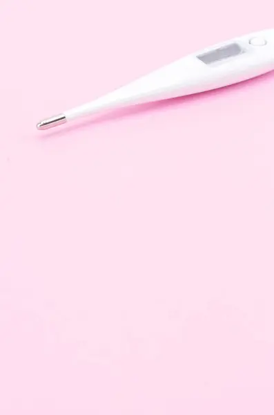 A vertical shot of digital thermometer on pink background with space for your text - disease control concept