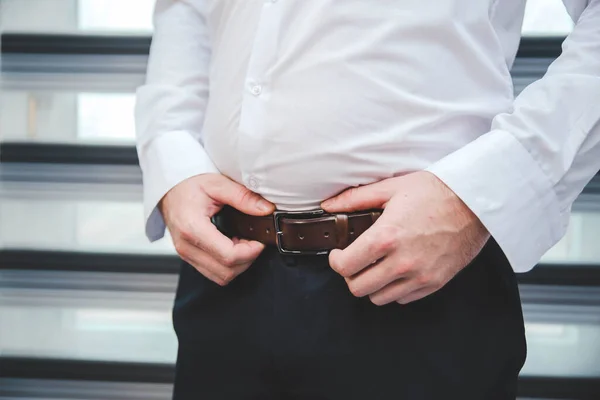 A male fixing his belt on the trousers