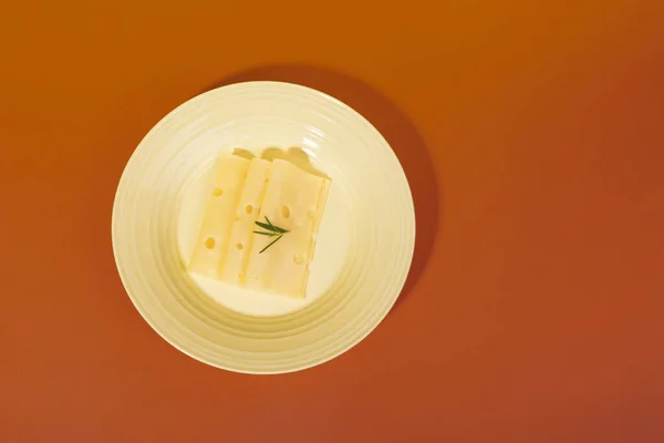 Вид Сверху Швейцарские Ломтики Сыра Розмарином Тарелке Изолированной Оранжевом Фоне — стоковое фото
