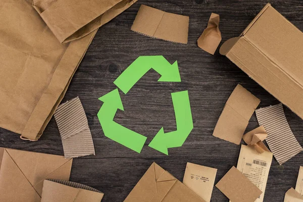 A top view of recycling sign and cardboard on wooden surface, recycling concept