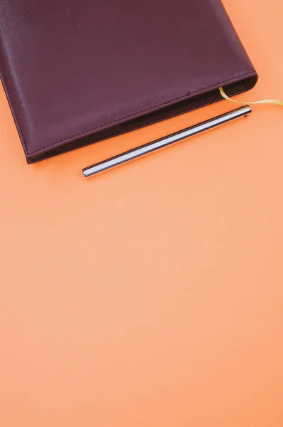 黄色のブックマークとオレンジの背景に孤立したペンを持つ黒のノートブックのトップビューの閉鎖 — ストック写真