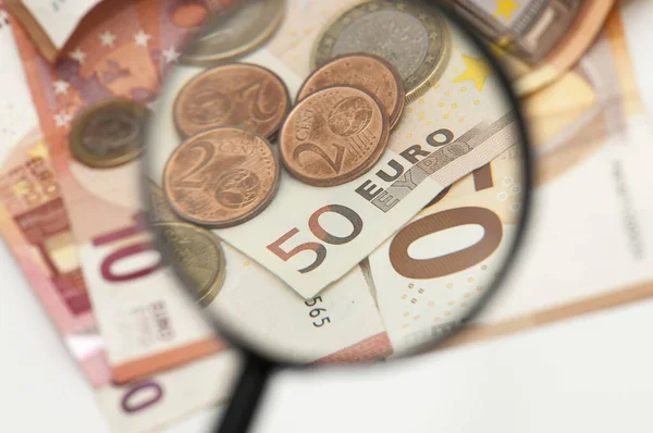 A magnifier finding euro coins on euro banknotes background, the concept of savings