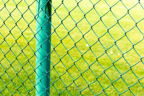 A closeup of chain-link fences in a field under the sunlight with a blurry background