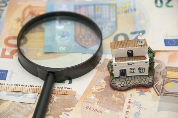 欧元钞票背景上的放大镜和小房子雕像 房地产评估的概念 — 图库照片