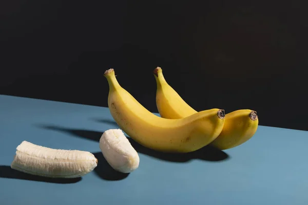Par Plátanos Uno Cortado Por Mitad Sobre Una Superficie Azul — Foto de Stock