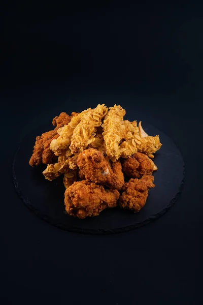 A closeup shot of a black serving plate full of chicken nuggets and crispy fried chicken