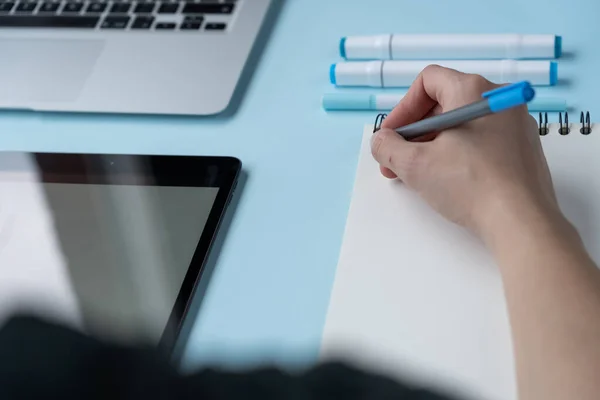 青い机の上のタブレットとノートパソコンを使ってメモをとる者の高い角度のショット — ストック写真