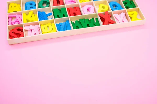 盒子里有许多彩色的木制字母 放在粉色的表面上 — 图库照片