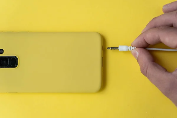 Seseorang Memasukkan Kawat Headphone Dalam Telepon Pada Permukaan Kuning Dengan — Stok Foto
