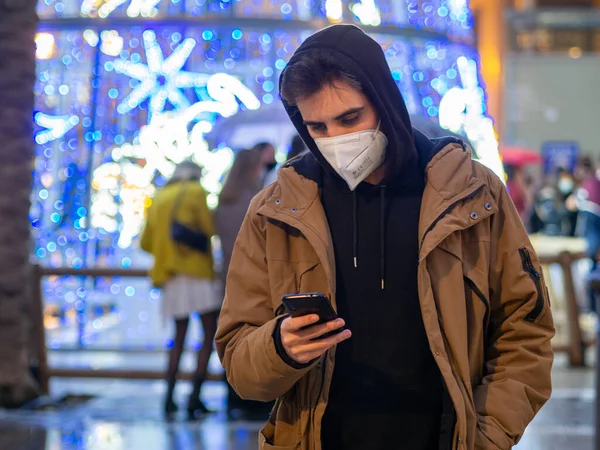 Ένας Νεαρός Άνδρας Μια Μάσκα Προσώπου Έλεγχο Του Τηλεφώνου Του — Φωτογραφία Αρχείου