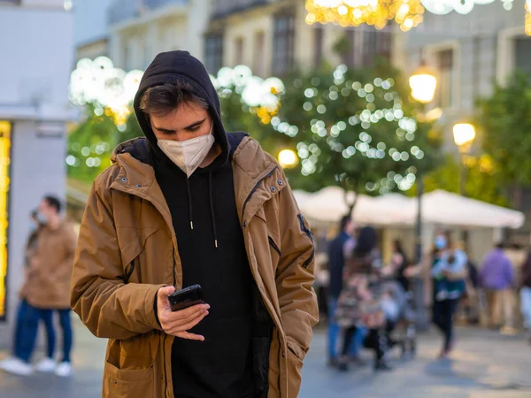 Een Jonge Man Een Gezichtsmasker Controleert Zijn Telefoon Tijdens Kerst — Stockfoto