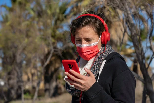 Μια Γυναίκα Που Φοράει Προστατευτική Μάσκα Και Ακουστικά Κοιτάζοντας Τηλέφωνό — Φωτογραφία Αρχείου