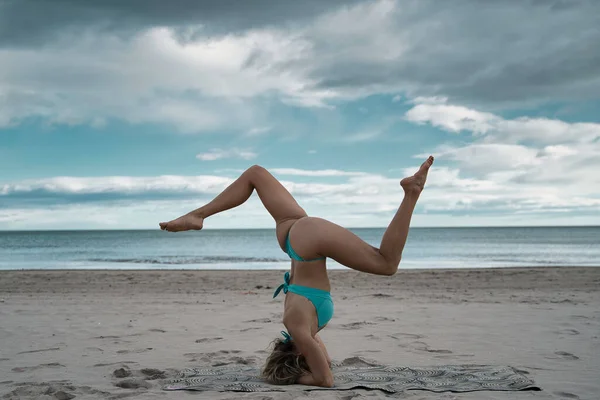 一个穿着泳衣的金发模特站在海滩上做瑜伽的漂亮照片 站在她的头上 — 图库照片