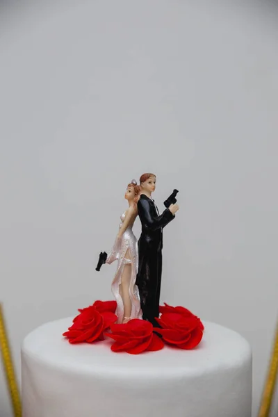 白のウェディングケーキの上に銃を保持しているいくつかの人形の垂直クローズアップショット — ストック写真
