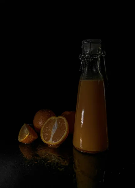 Narancsok Egy Üveg Gyümölcslé Függőleges Közelsége Fekete Alapon Árnyékok Alatt — Stock Fotó