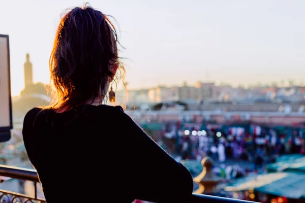 A back view of a female leaning on a balcony railing enjoying a beautiful city view