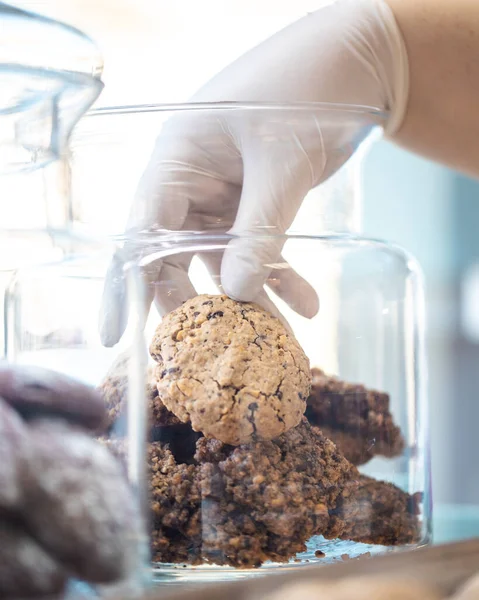 A vertical shot of a gloved hand taking out a cookie from a jar