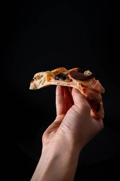 Pionowe Ujęcie Osoby Trzymającej Kawałek Pizzy Czarnym Tle — Zdjęcie stockowe