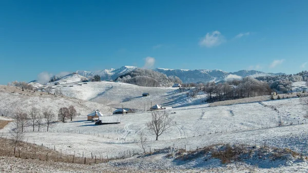 在蓝色天空下被群山环绕的乡村风景中 在冬季的场景中 有几栋房子 — 图库照片
