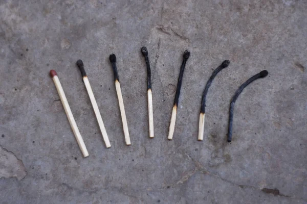 A top view of different stages of burned fire matches on a concrete surface - burn out concept