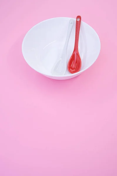 ピンクの背景を持つ白いボウルに置かれた赤いスプーンの高角度垂直ショット — ストック写真