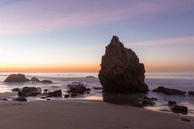 The wavy ocean hitting the rocky El Matador Beach gleaming under the sunset in Malibu, California clipart